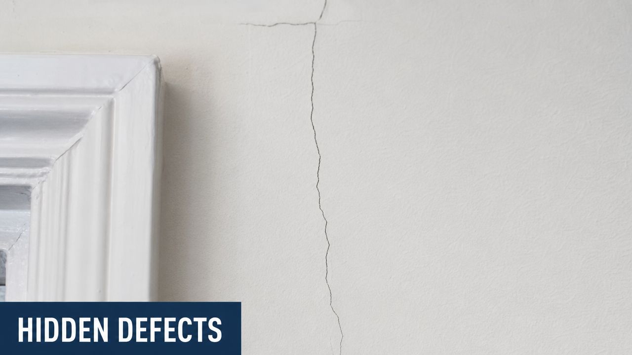 A close-up view of a vertical drywall crack near a wooden window frame inside a home.